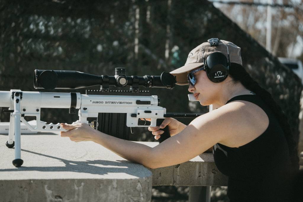 A woman aiming down the sights of a cheytac intervention sniper rifle